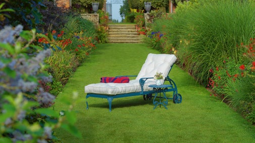 Garden lounger on grass surrounded by plants blooming in spring